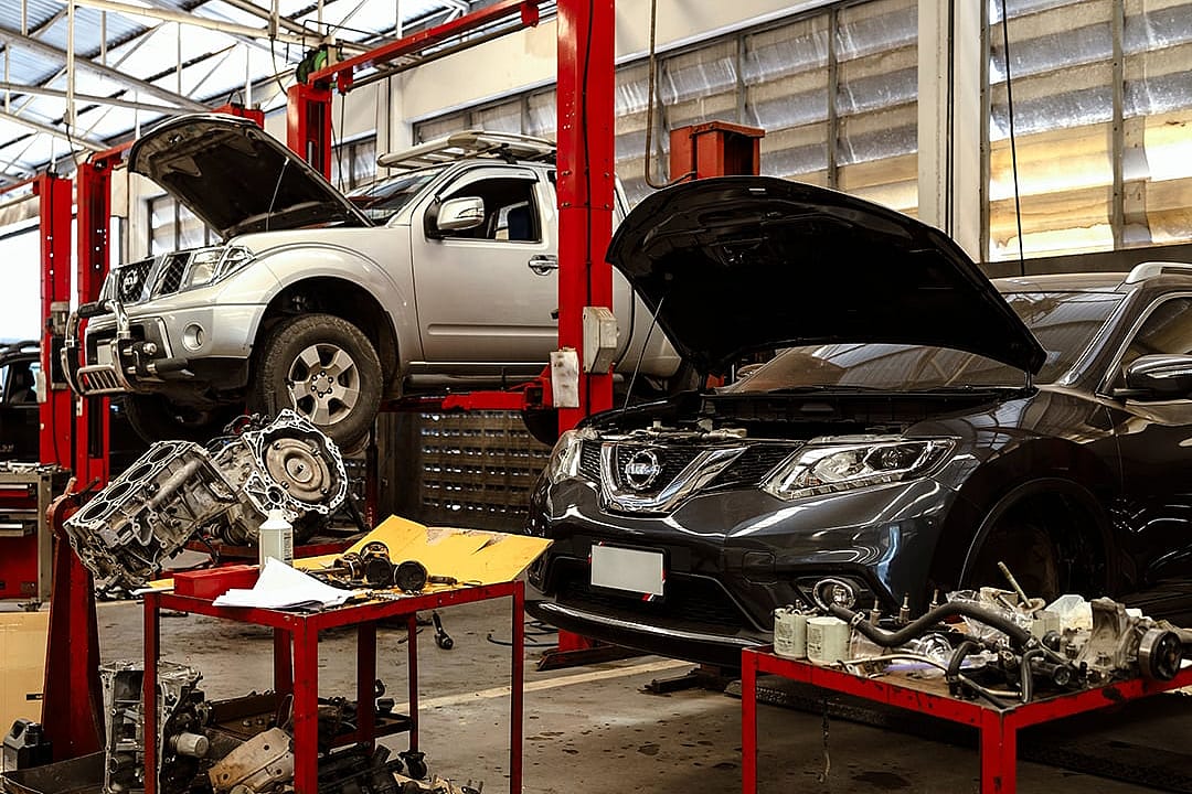 Cars seen on lifts with tools scattered around inside an automotive maintenance and repair shop.